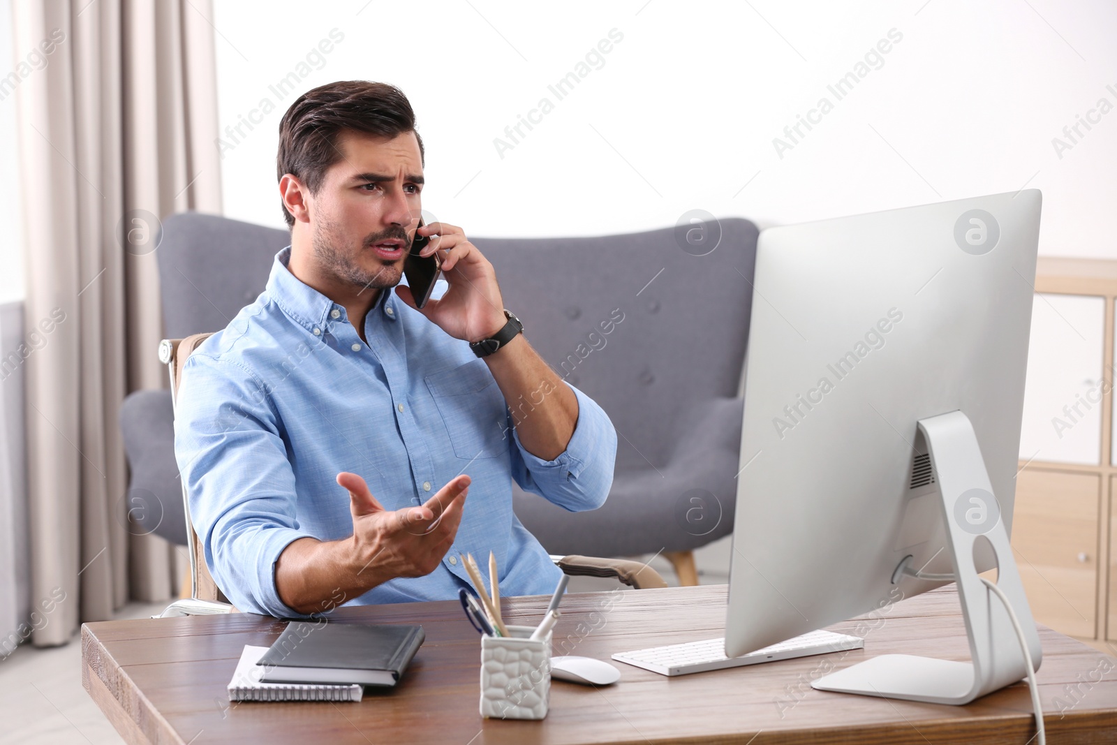 Photo of Handsome young man working with smartphone and computer at table in office