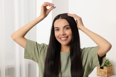 Photo of Beautiful woman applying hair serum in room. Cosmetic product