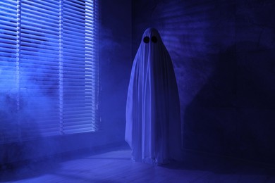 Creepy ghost. Woman covered with sheet near window in blue light