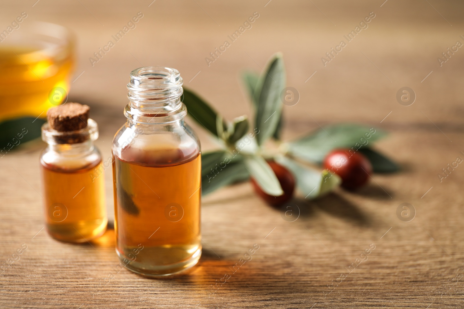 Photo of Glass bottles with jojoba oil on wooden table. Space for text