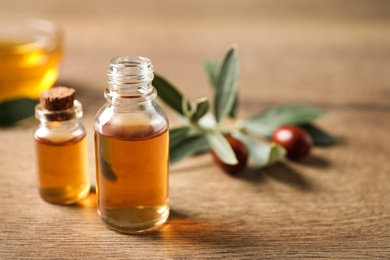 Glass bottles with jojoba oil on wooden table. Space for text