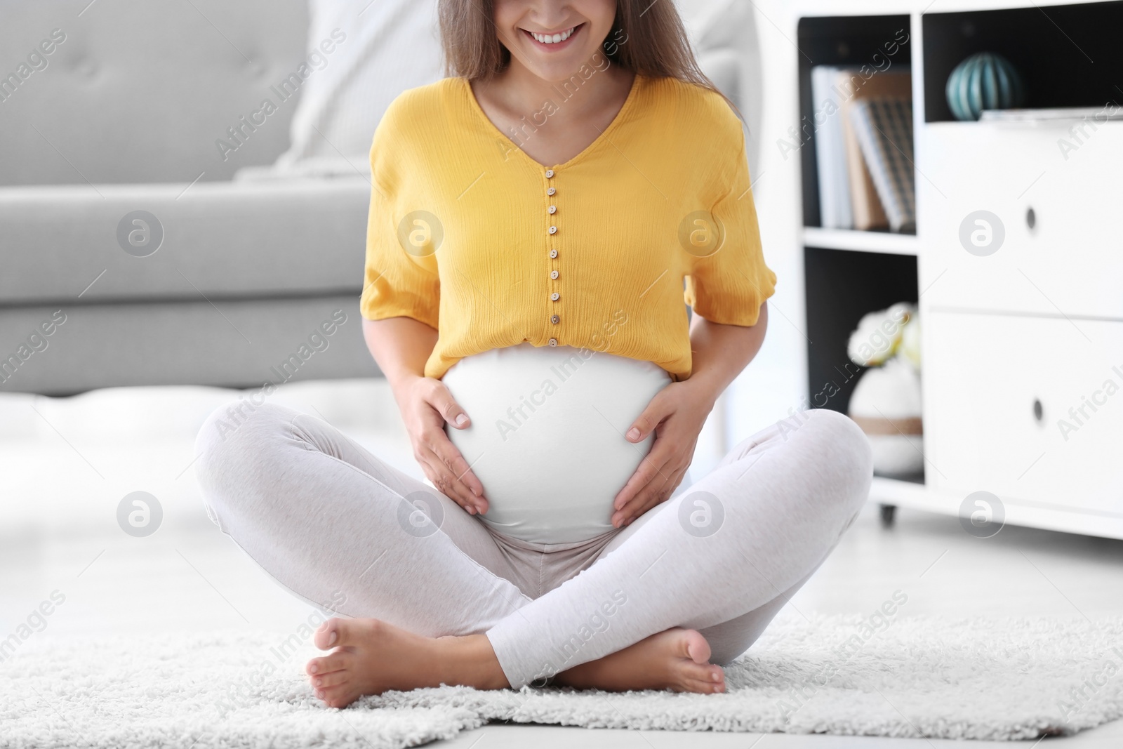 Photo of Pregnant woman sitting on floor at home, closeup