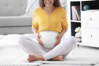 Pregnant woman sitting on floor at home, closeup