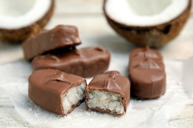 Photo of Delicious milk chocolate candy bars with coconut filling on white wooden table, closeup