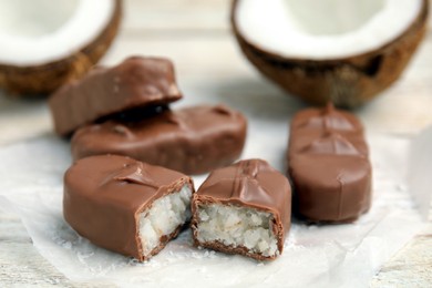 Delicious milk chocolate candy bars with coconut filling on white wooden table, closeup