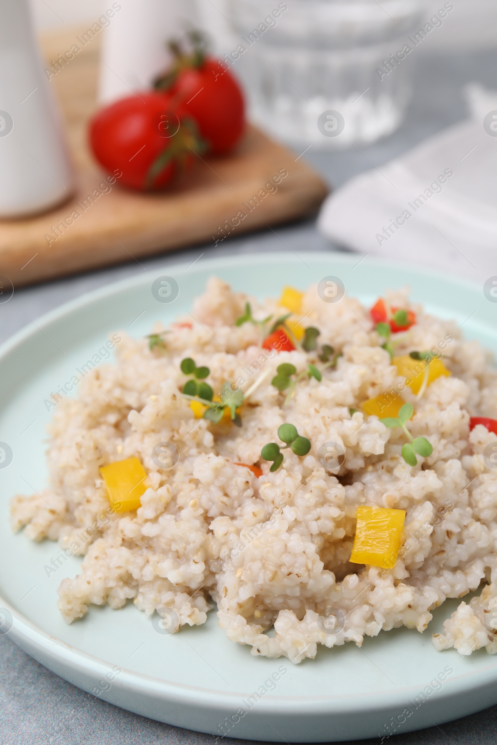 Photo of Delicious barley porridge with vegetables and microgreens on table, closeup