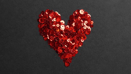 Photo of Red sequins in shape of heart on black background, flat lay