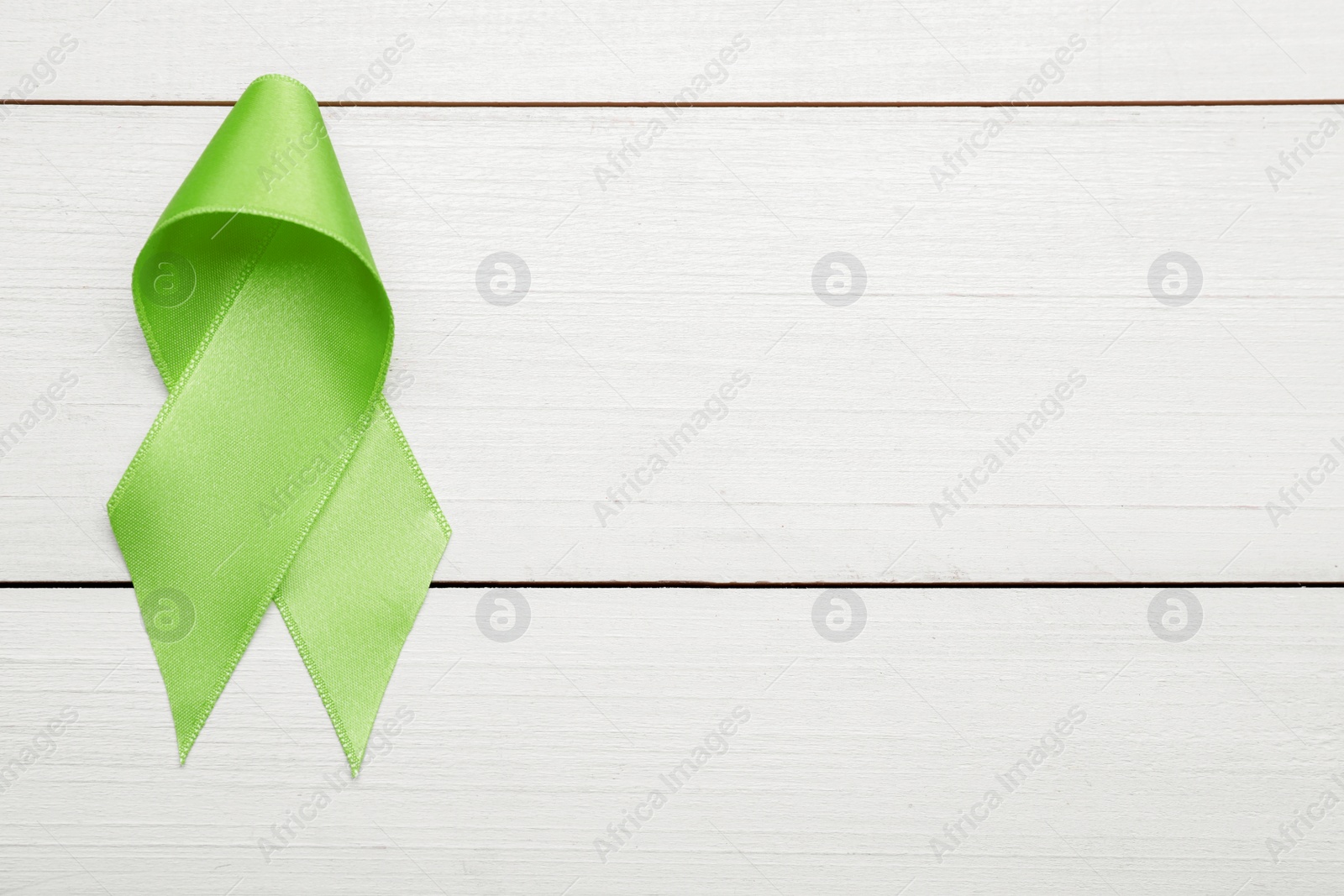 Photo of World Mental Health Day. Green ribbon on white wooden background, top view with space for text