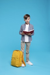 Photo of Cute schoolboy with book on light blue background