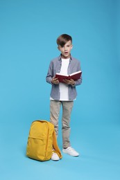 Cute schoolboy with book on light blue background