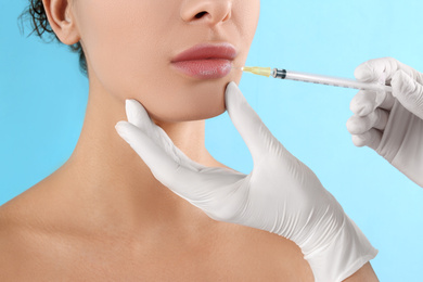 Woman getting lip injection on light blue background, closeup