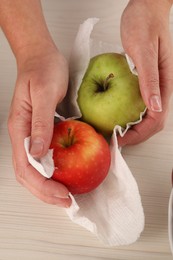 Photo of Woman wiping apples with paper towel at light wooden table, top view