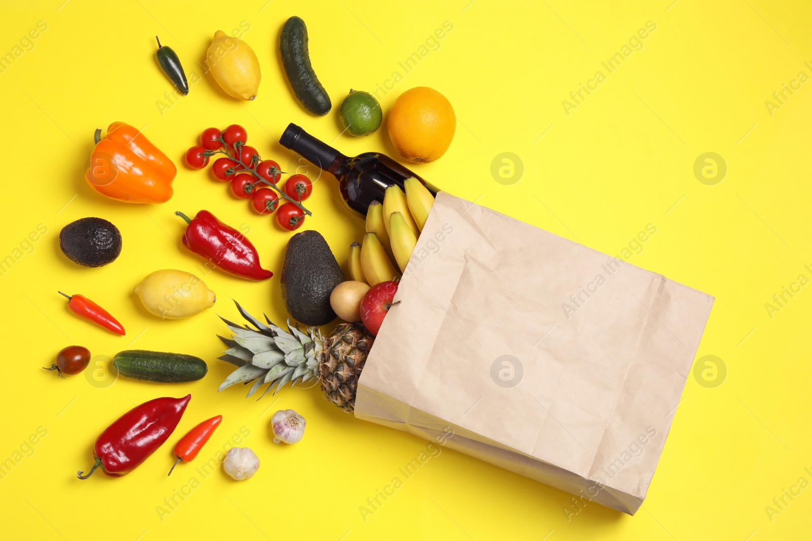 Photo of Shopping paper bag with different groceries on yellow background, flat lay