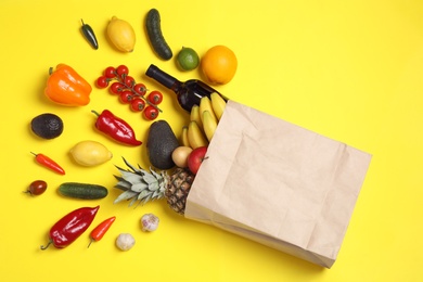 Shopping paper bag with different groceries on yellow background, flat lay