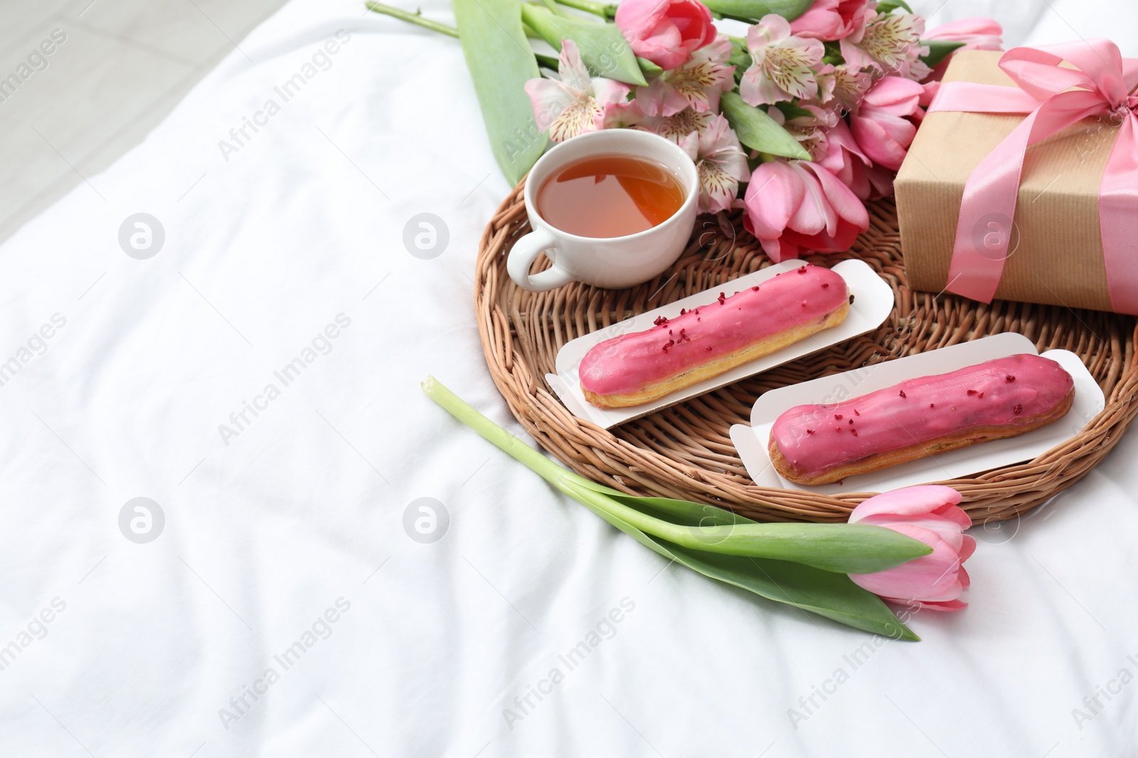 Photo of Tasty breakfast. Delicious eclairs, tea, flowers and gift box on bed, space for text