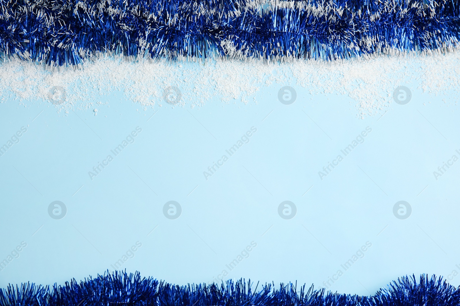 Photo of Shiny tinsel and snow on light blue background, flat lay. Space for text