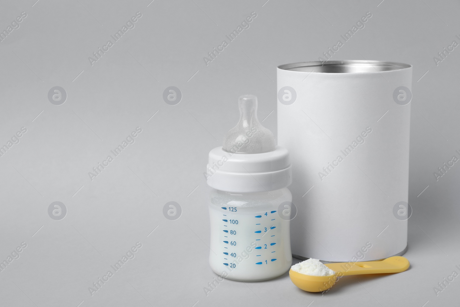 Photo of Blank can of powdered infant formula with scoop and feeding bottle on light grey background, space for text. Baby milk