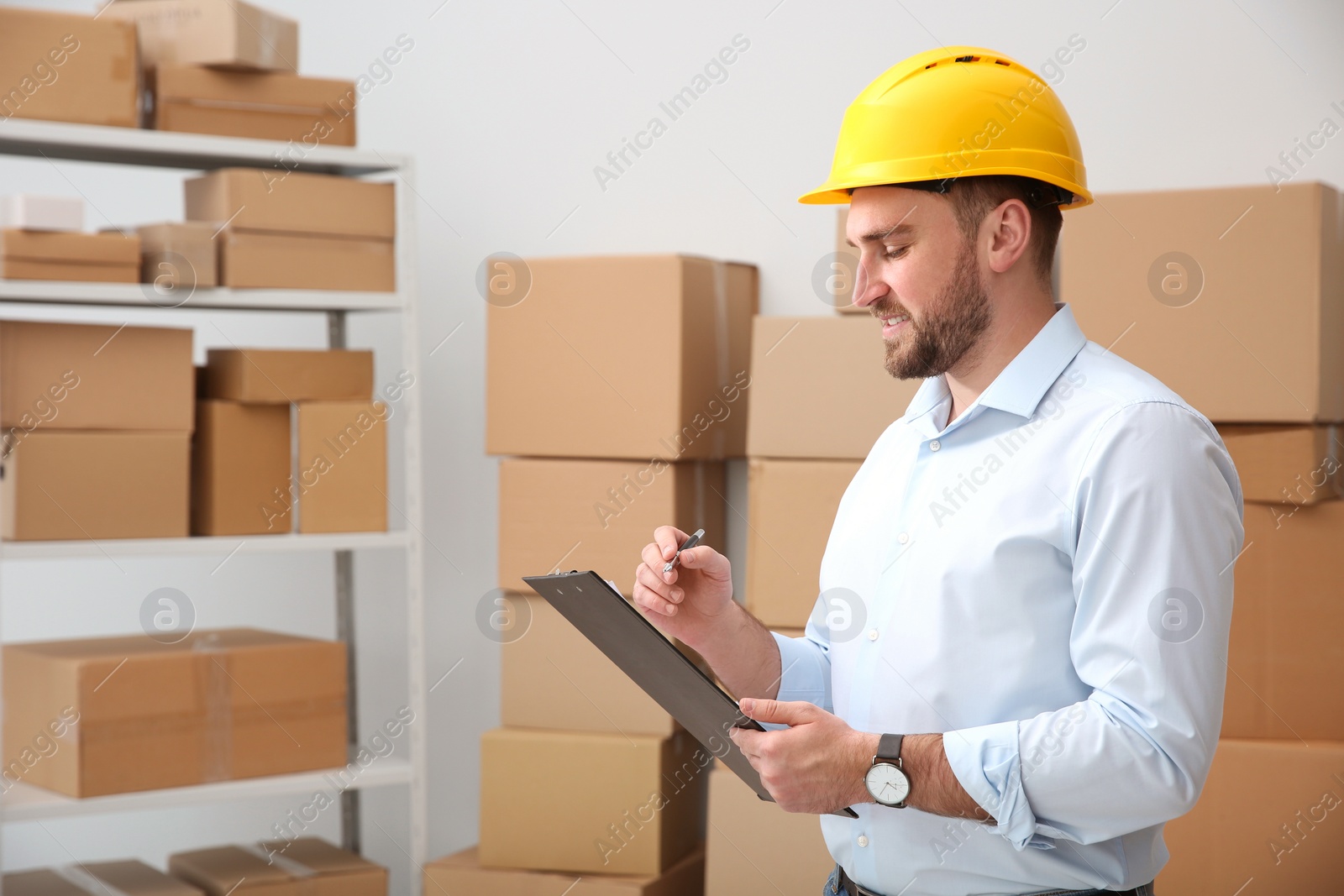 Photo of Young man with clipboard near cardboard boxes at warehouse