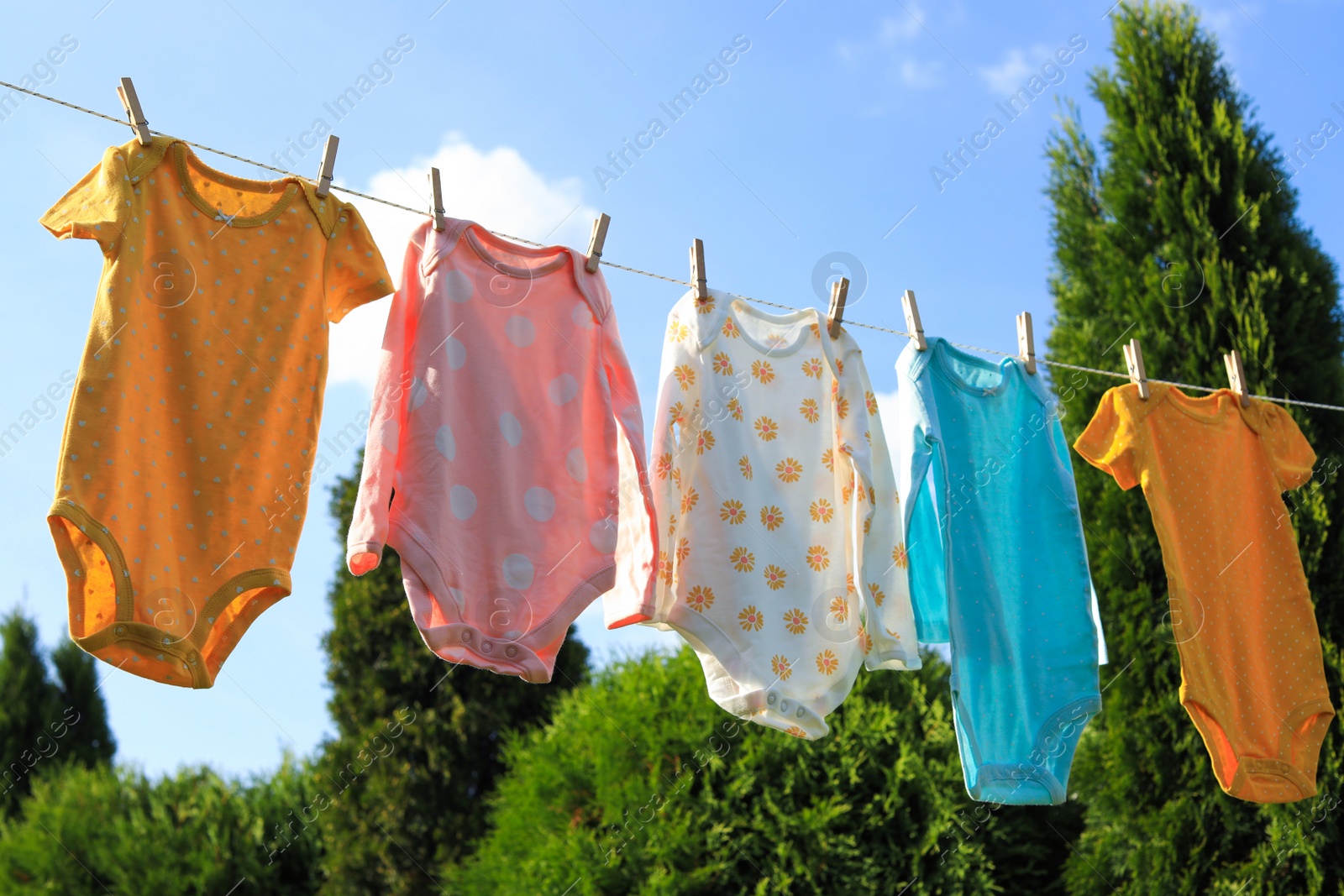 Photo of Clean baby onesies hanging on washing line in garden. Drying clothes