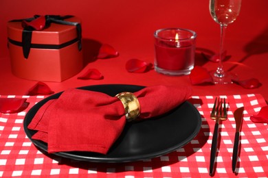 Photo of Beautiful table setting with gift box and burning candle on red table for romantic dinner