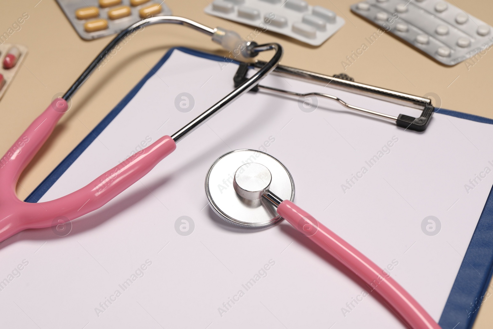 Photo of Stethoscope, clipboard and pills on beige background, closeup. Medical tool