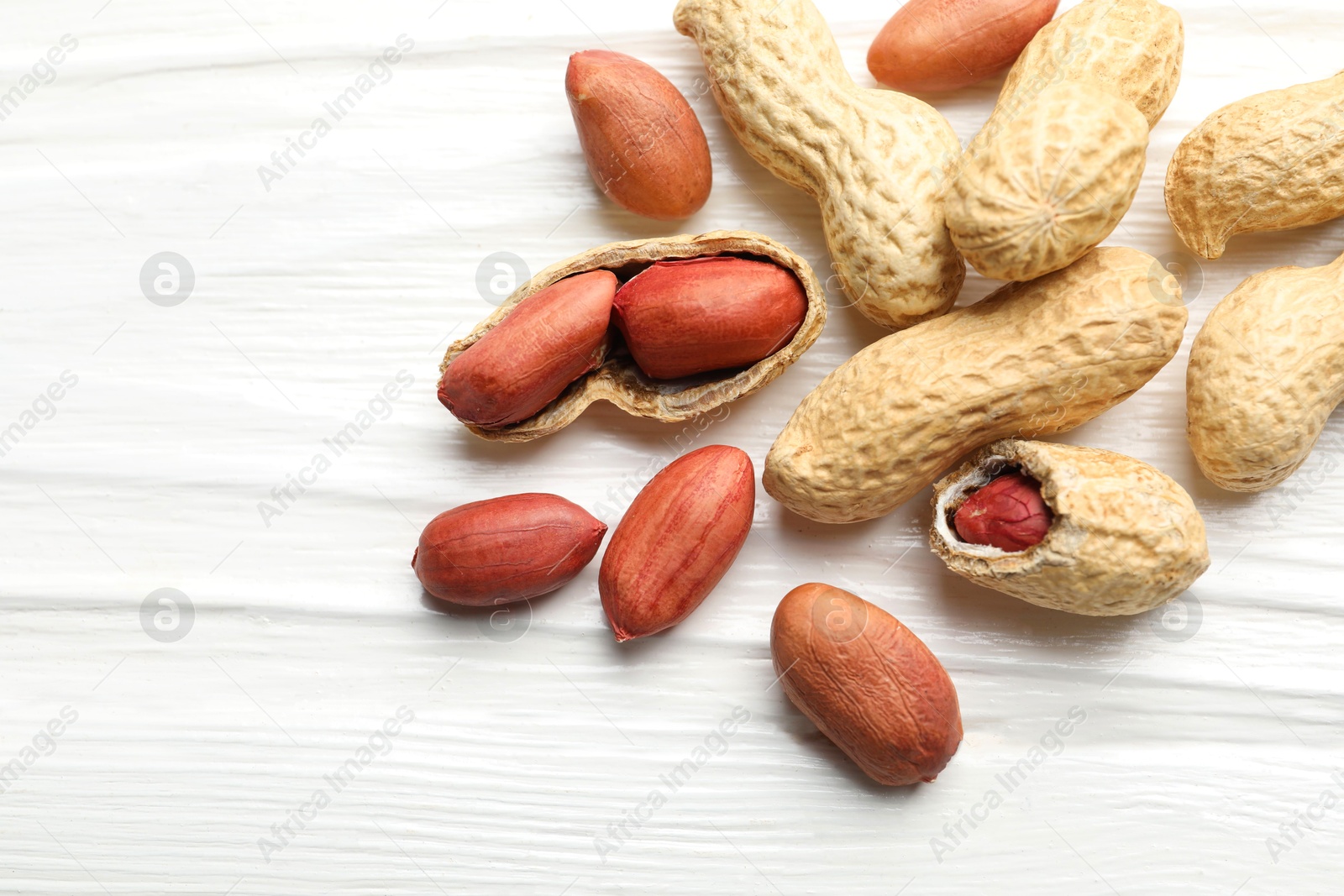 Photo of Fresh unpeeled peanuts on white wooden table, flat lay. Space for text