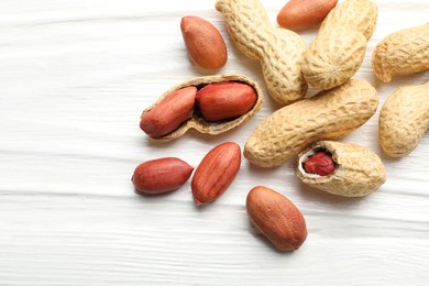 Photo of Fresh unpeeled peanuts on white wooden table, flat lay. Space for text