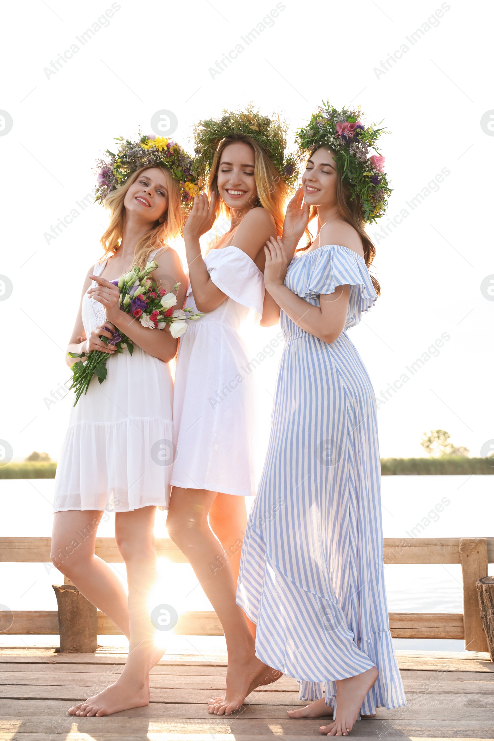 Photo of Young women wearing wreaths made of beautiful flowers on pier near river