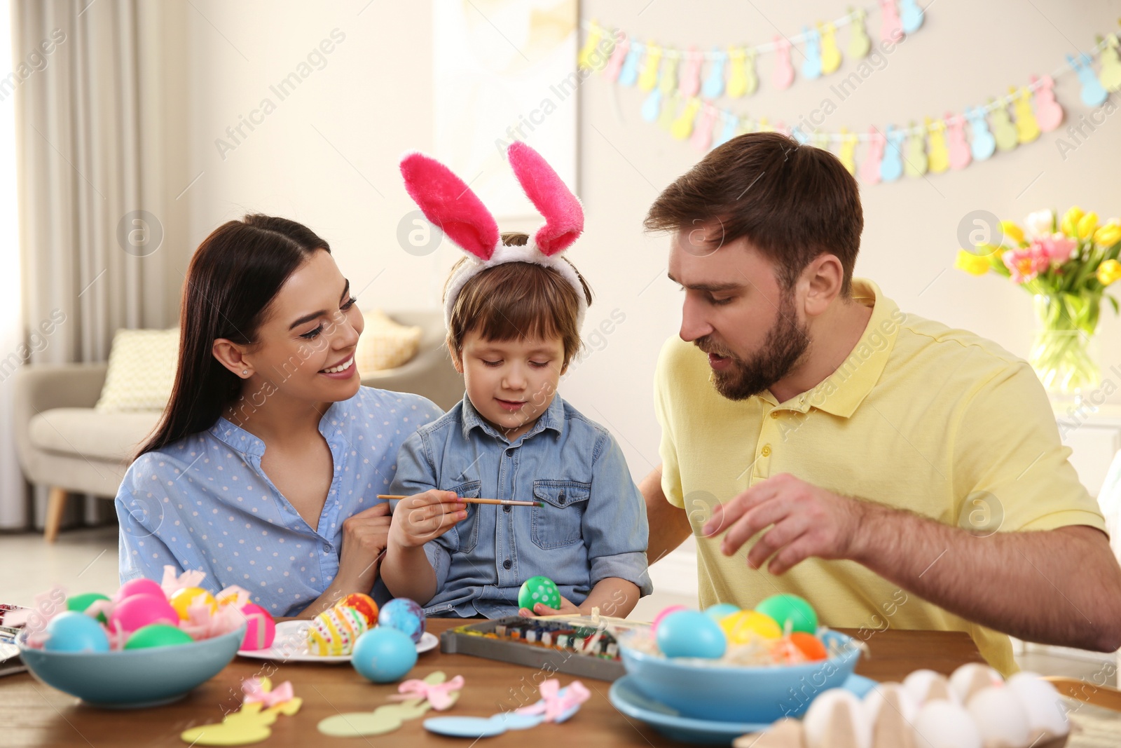 Photo of Happy family painting Easter eggs at table indoors