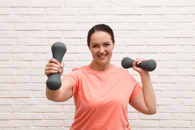 Photo of Happy overweight woman doing exercise with dumbbells near white brick wall
