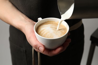 Woman pouring milk into cup of coffee on grey background, closeup