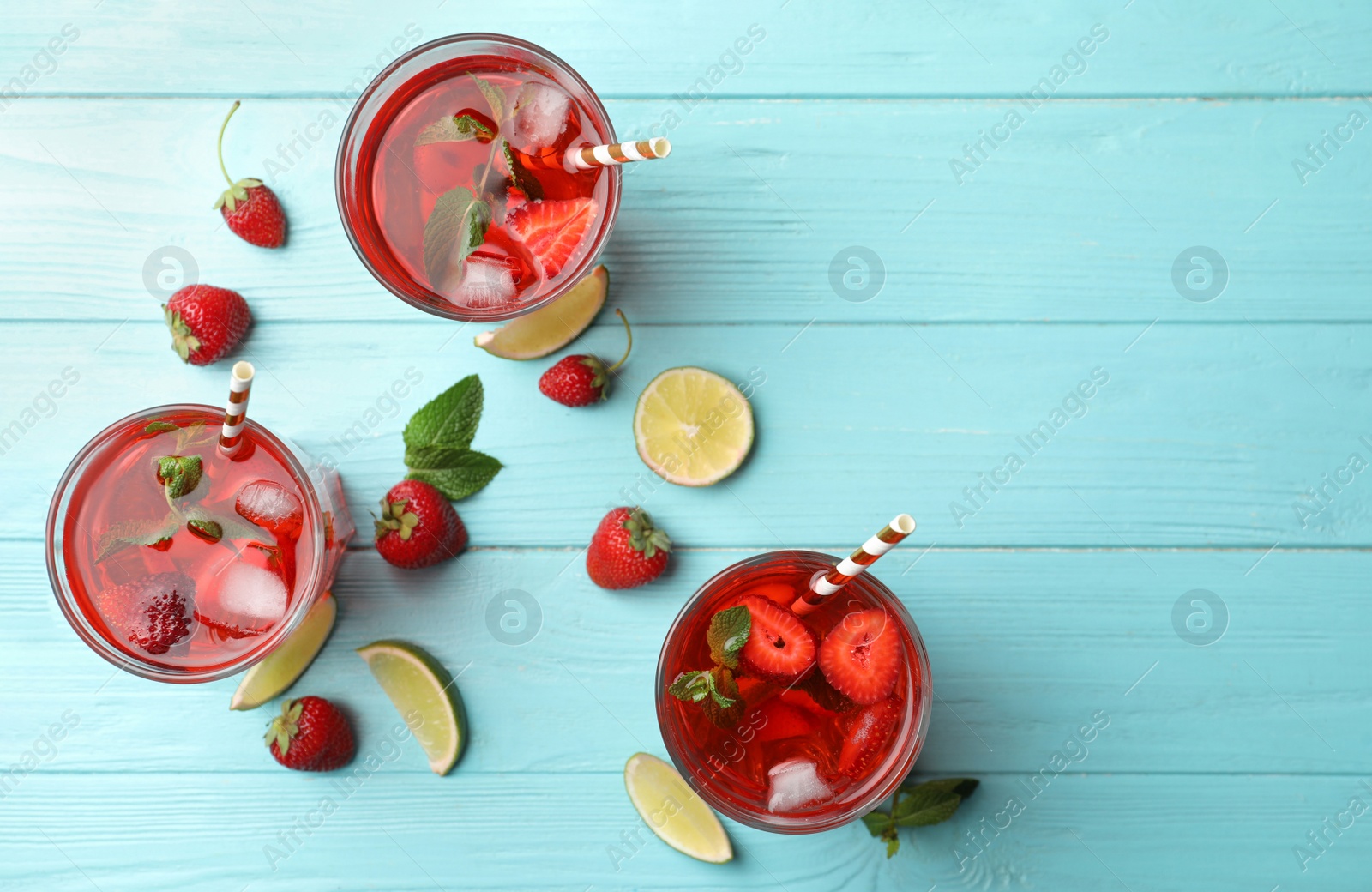 Photo of Refreshing drink with strawberry and lime on light blue wooden table, flat lay. Space for text