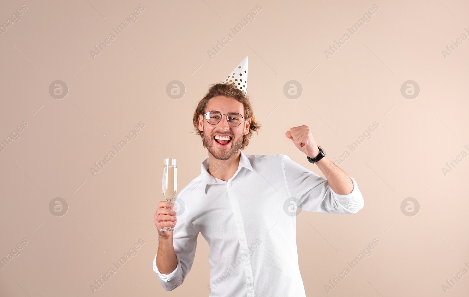 Photo of Portrait of happy man with party cap and champagne in glass on color background