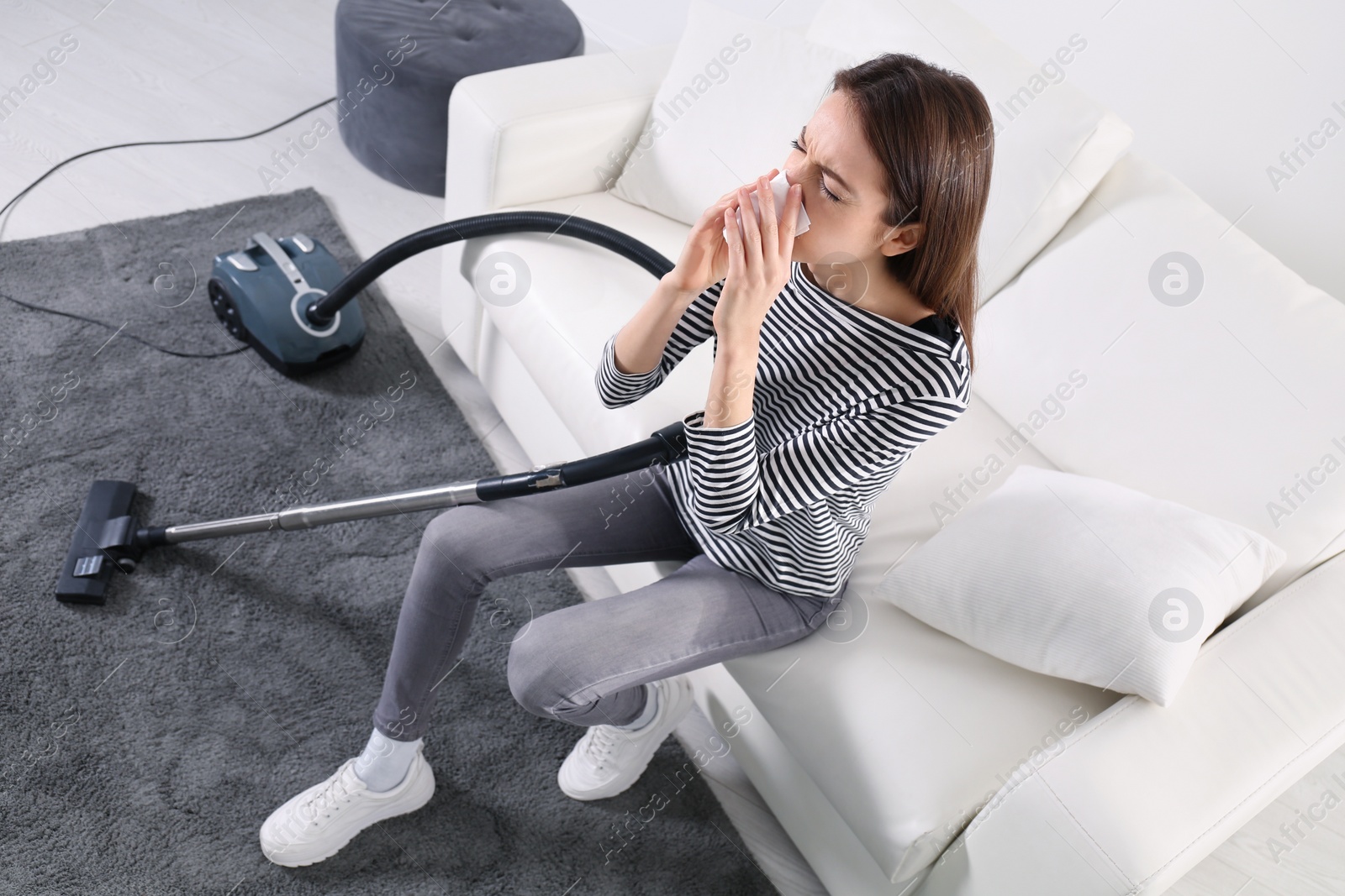 Photo of Young woman suffering from dust allergy while vacuuming house