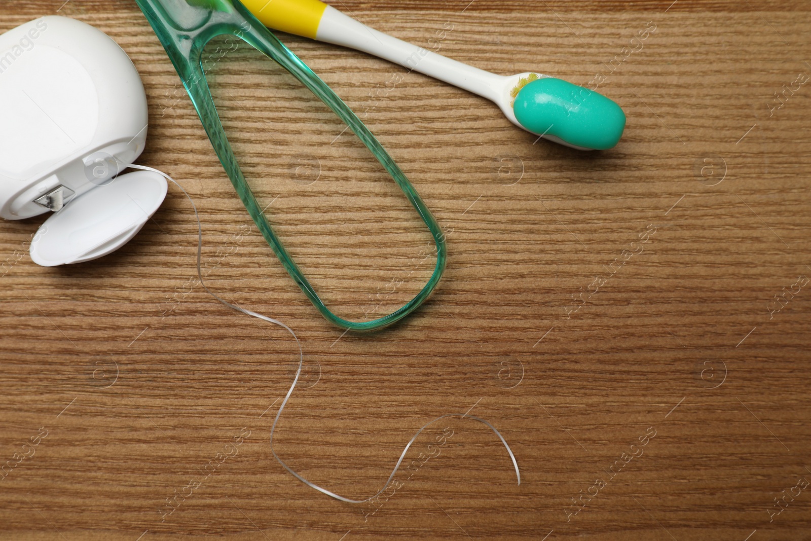 Photo of Green tongue cleaner, dental floss and toothbrush with paste on wooden table, flat lay