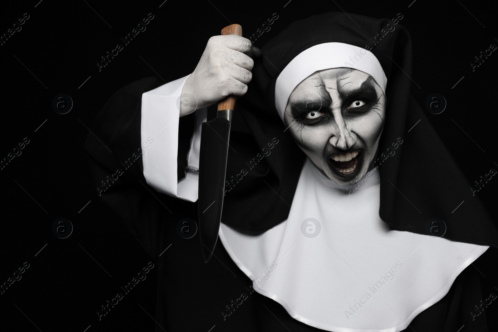 Photo of Scary devilish nun with knife on black background. Halloween party look