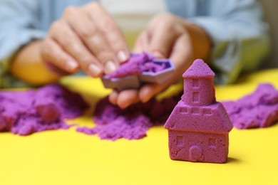 Photo of Woman playing with kinetic sand at yellow table, selective focus