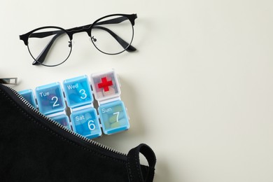Eyeglasses and handbag with pill box on white background, flat lay. Space for text