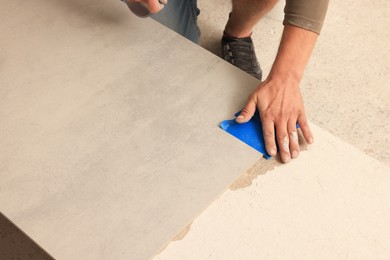 Photo of Worker preparing tile for installation indoors, closeup