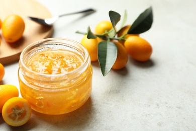 Photo of Delicious kumquat jam in jar and fresh fruits on light grey table, space for text