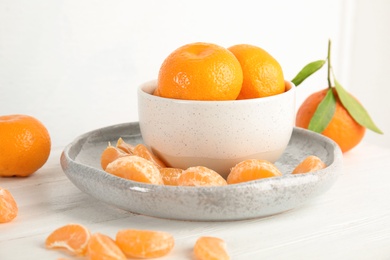 Photo of Plate and bowl with ripe tangerines on table