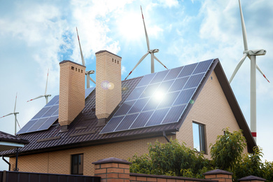 Image of Wind turbines near house with installed solar panels on roof. Alternative energy source