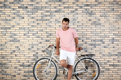 Photo of Handsome young hipster man with bicycle on brick wall background