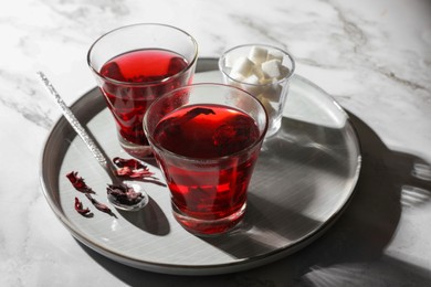 Photo of Delicious hibiscus tea, sugar cubes and dry roselle petals on white marble table