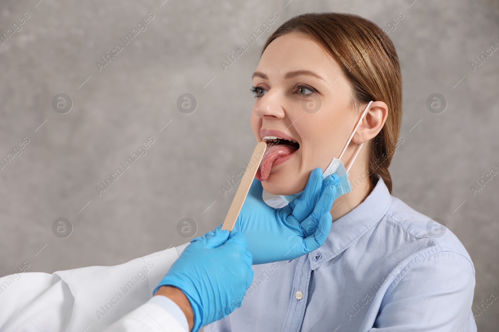 Photo of Doctor examining woman`s oral cavity with tongue depressor indoors. Space for text