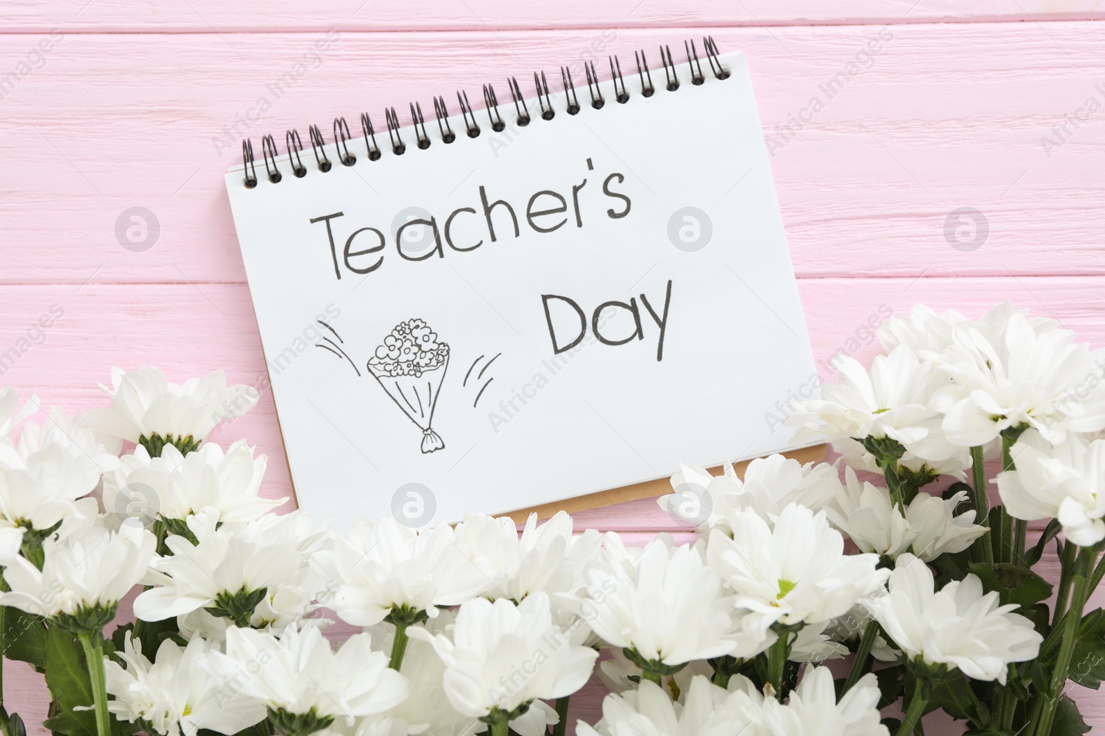 Photo of Beautiful flowers and notebook with words TEACHER'S DAY on pink wooden background, flat lay