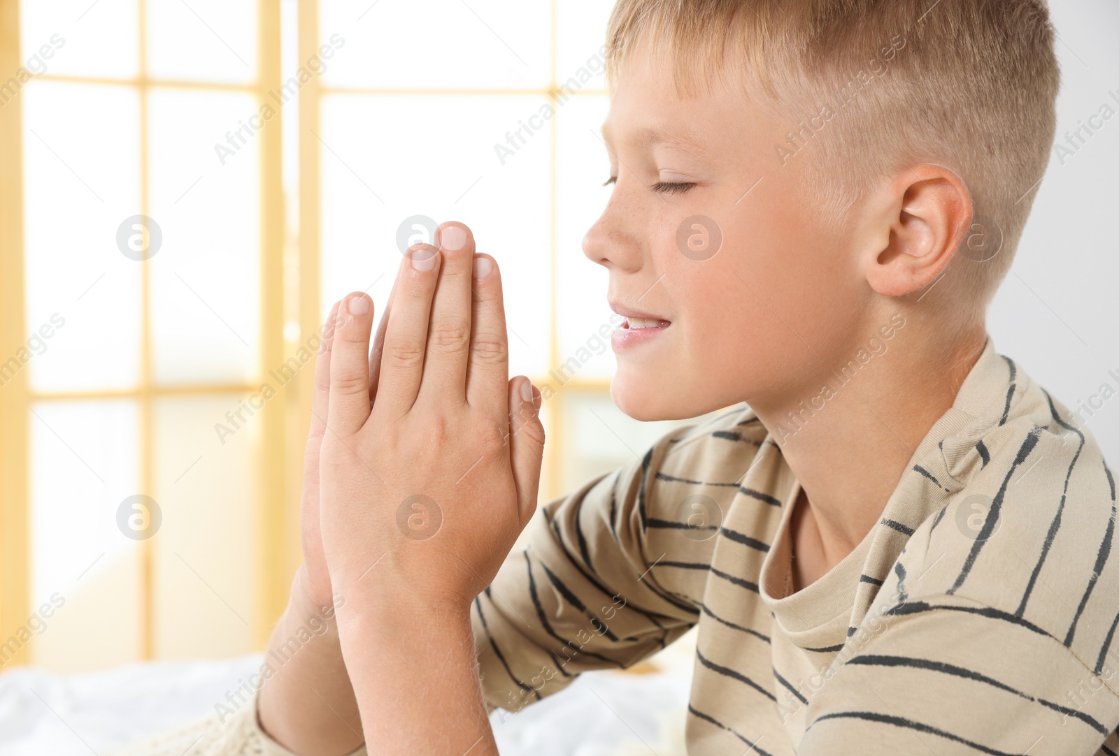 Photo of Boy with clasped hands praying indoors, space for text