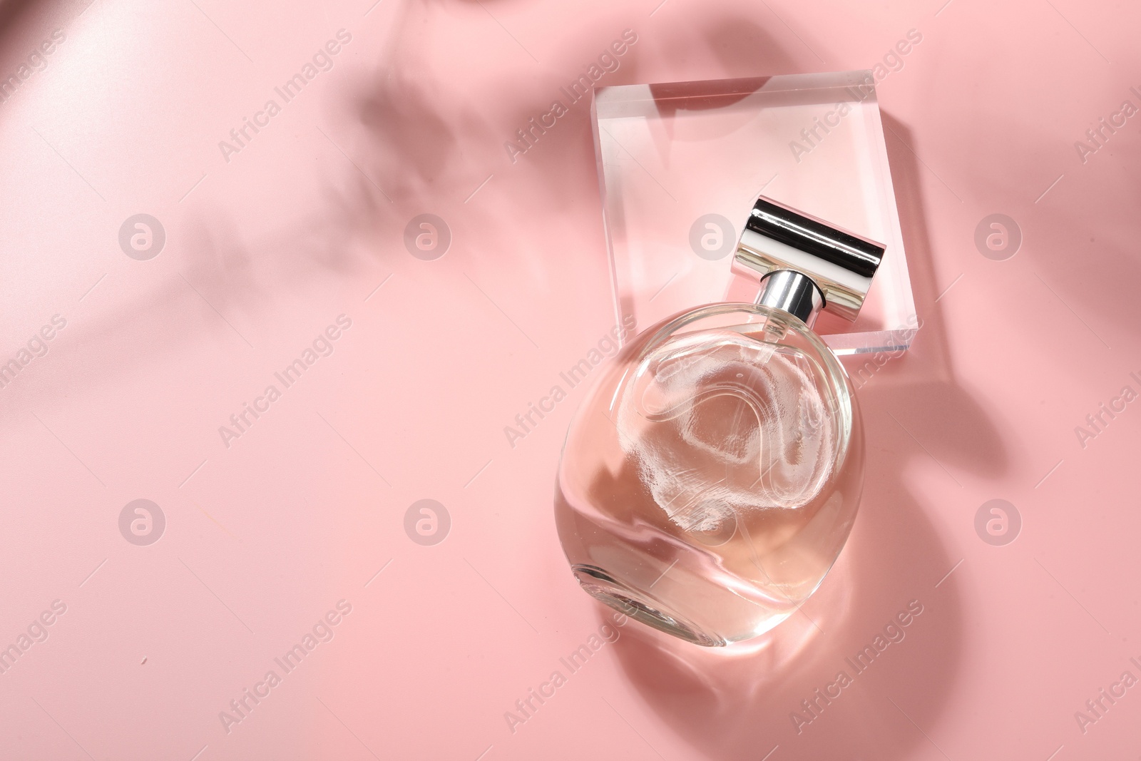 Photo of Bottle of luxury women's perfume in sunlight on pink background, above view. Space for text