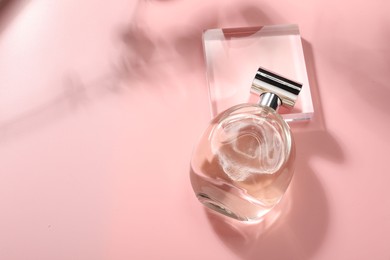 Bottle of luxury women's perfume in sunlight on pink background, above view. Space for text