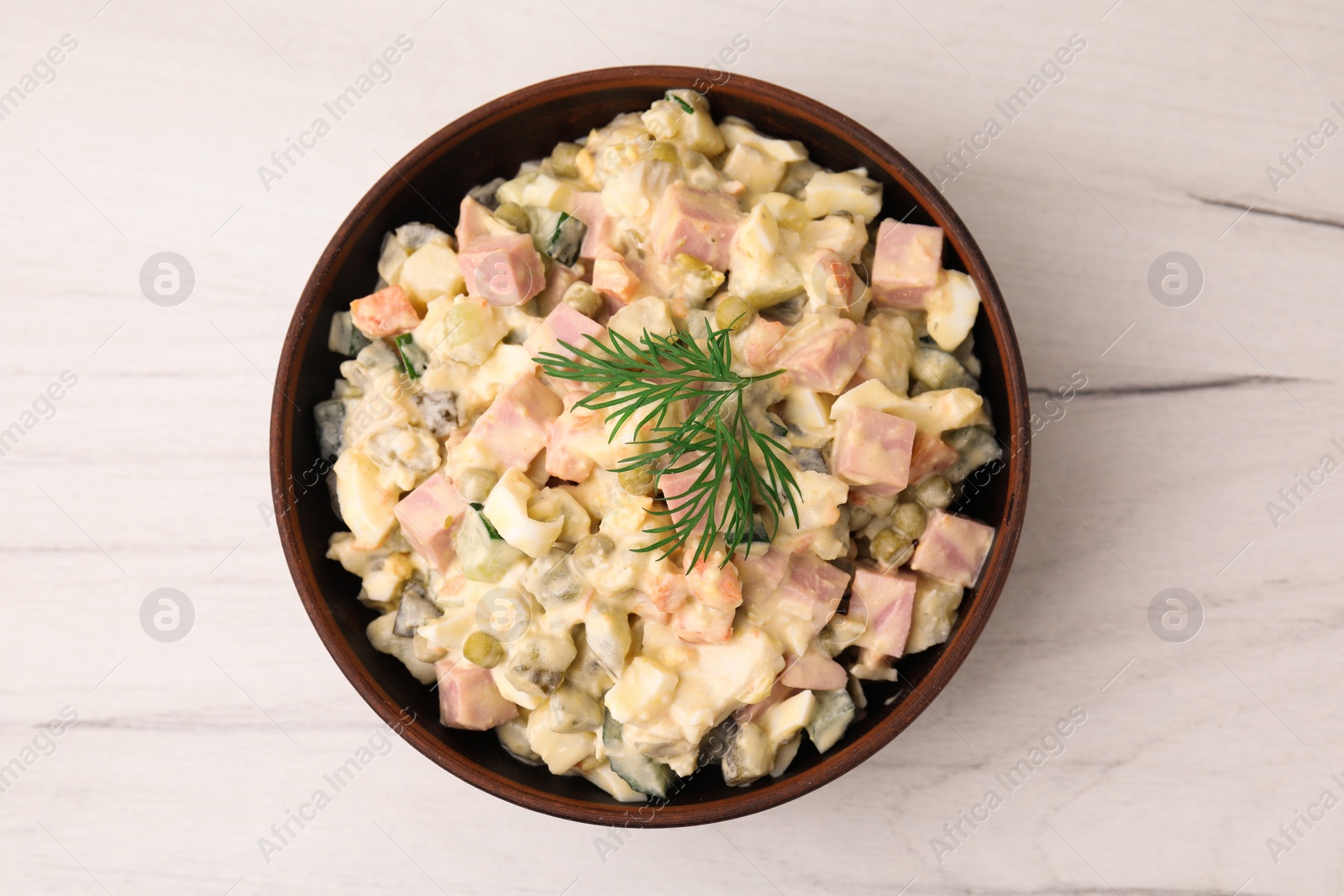 Photo of Tasty Olivier salad with boiled sausage in bowl on white wooden table, top view